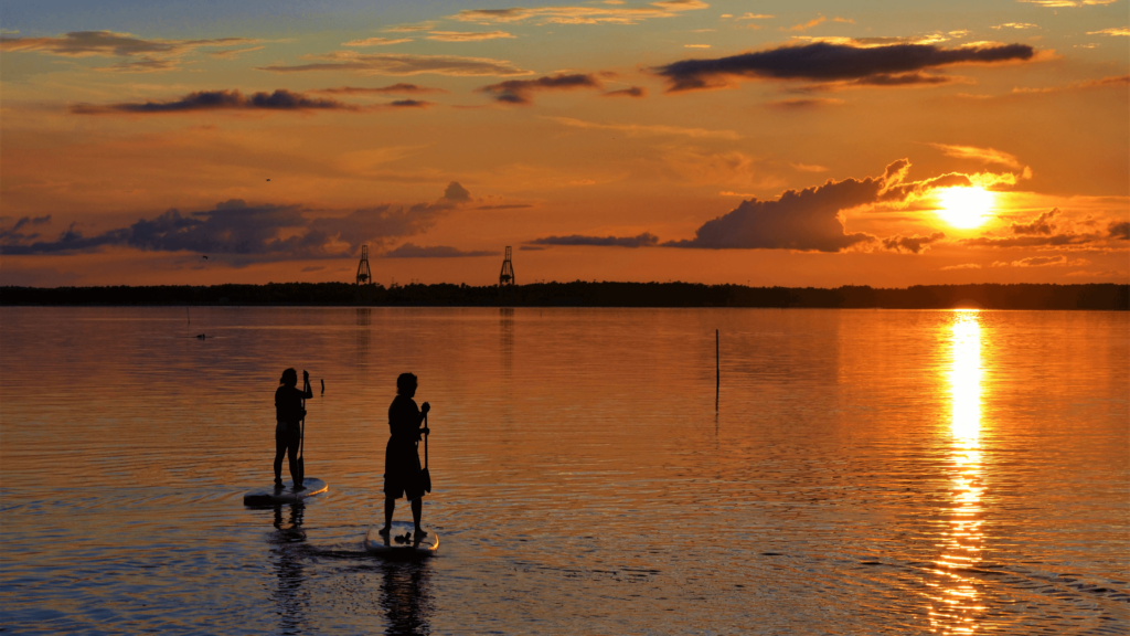 Two people paddleboarding into an orange sunset